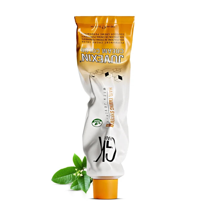 GK Hair Juvexin Cream Color 100 ml tube standing on its orange cap, with green leaves and small white blossoms at its base