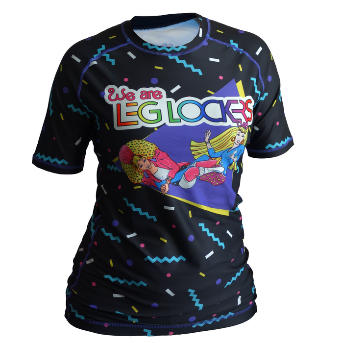 The Retro Grappler Leglockers Barbie Parody Rash Guard is a black, short-sleeve, four-way stretch shirt with colorful geometric patterns and We are LEG LOCKES above cartoon characters doing a wrestling move.