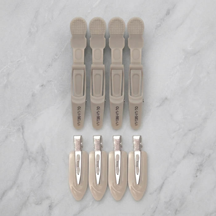 Four Olla Bella Crocodile Clips and four Olla Bella Creaseless Clips from the Olla Bella Mane Master Hair Clip Set arranged in two rows of two on a marble background.