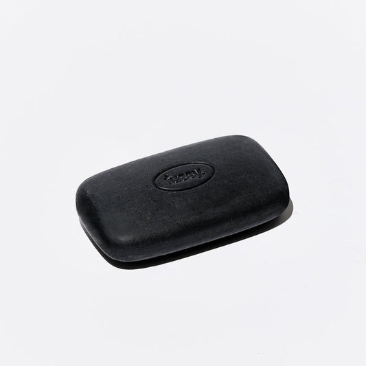 One singular, black exfoliating bar from Fussy, set at an angle.