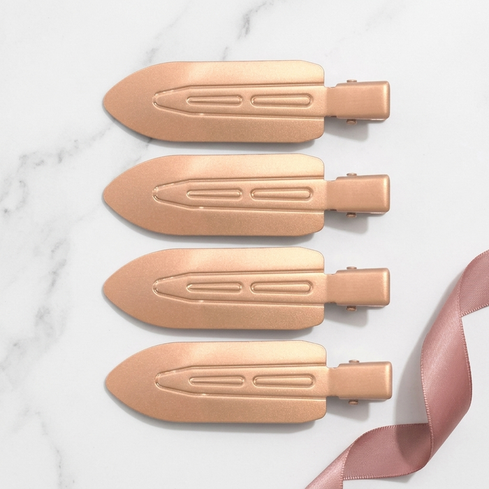 Four Olla Bella No-Crease Cuties - Creaseless Hair Clips arranged vertically on a white marble background with a pink ribbon in the bottom right corner.