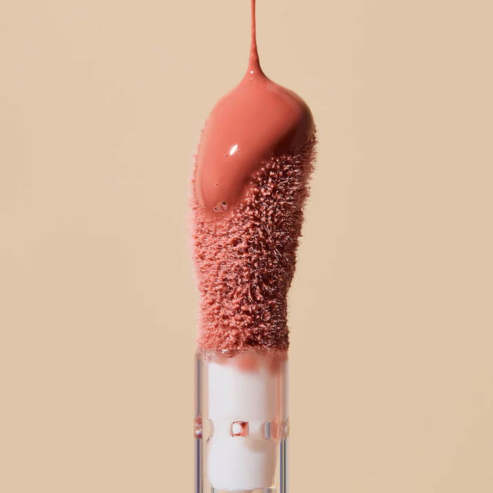 Makeup brush with pink bristles and a pink liquid tip on a beige background.