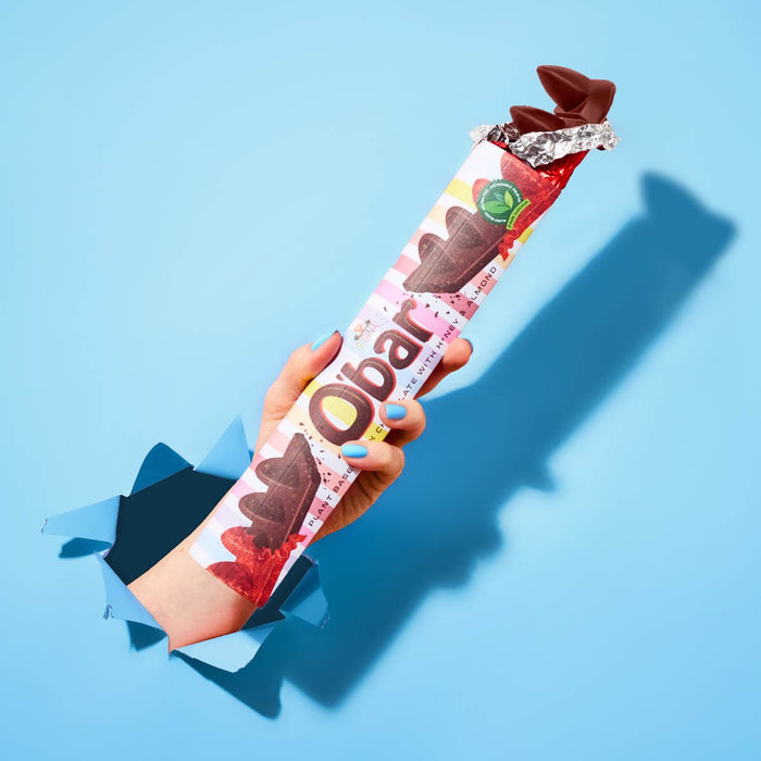 Vegan milk chocolate O'Bar held in a person's hand against a blue background.