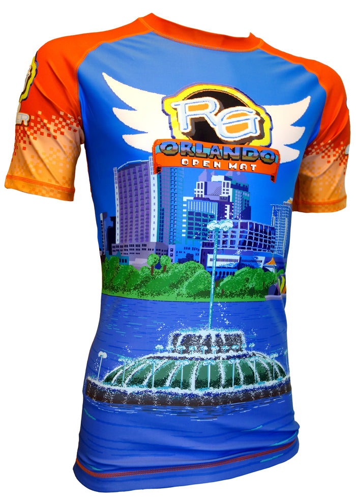 The Retro Grappler Orlando Open Mat Rash Guard is a colorful short-sleeve shirt with blue, orange, and yellow tones, featuring Orlando Open Mat text, a pixel art city skyline, and a large lake fountain graphic on the front.