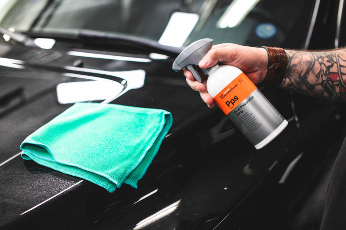 A person spraying KochChemie Panel Preparation Spray onto a green microfiber.