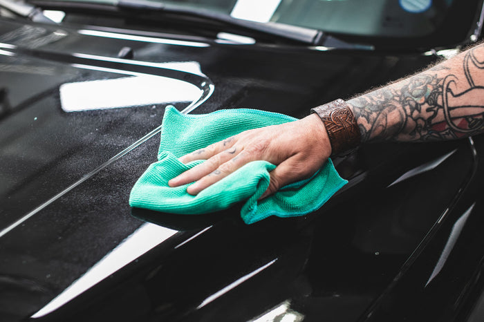 Person cleaning a car window with a green microfiber cloth.