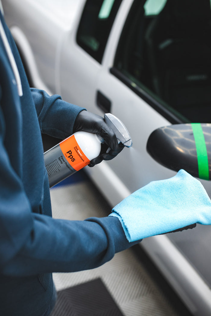 A person spraying KochChemie Panel Preparation Spray onto a blue microfiber.