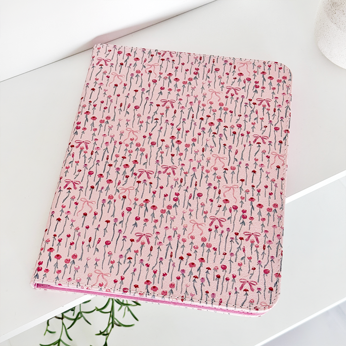 Peony Bow iPad case with a floral pattern on a white shelf next to a plain white pot.