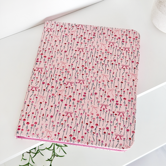 Peony Bow iPad case with a floral pattern on a white shelf next to a plain white pot.