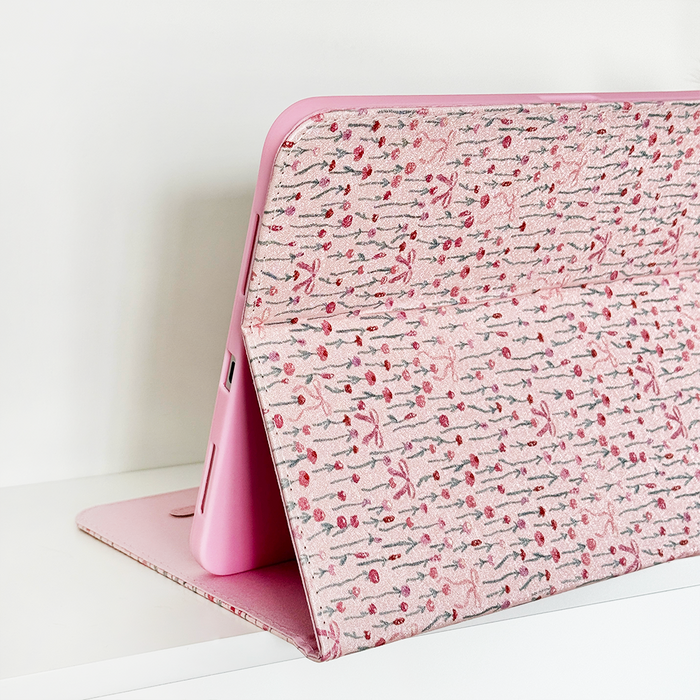 IPad in a pink floral Peony Bow case by Coconut Lane, propped open on a white surface.