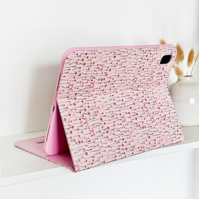 Pink Peony Bow iPad case props up a tablet on a white shelf next to a white vase holding dried grasses.