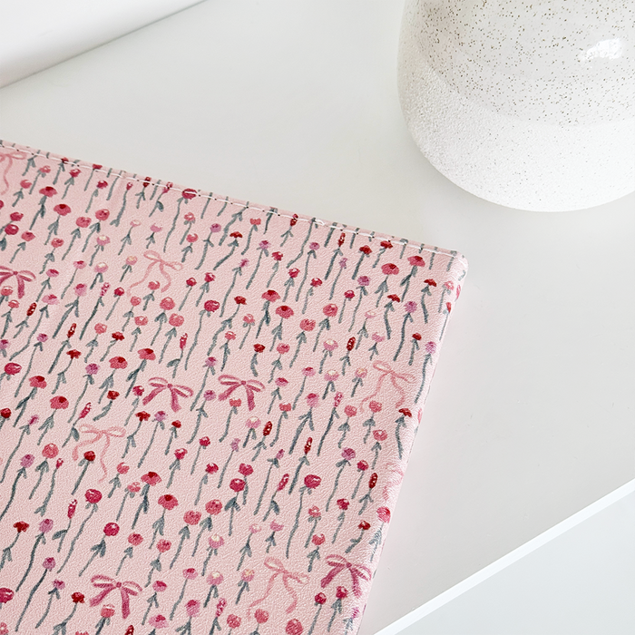 Coconut Lane Peony Bow iPad case with pink floral pattern next to a white speckled ceramic vase on a white surface.