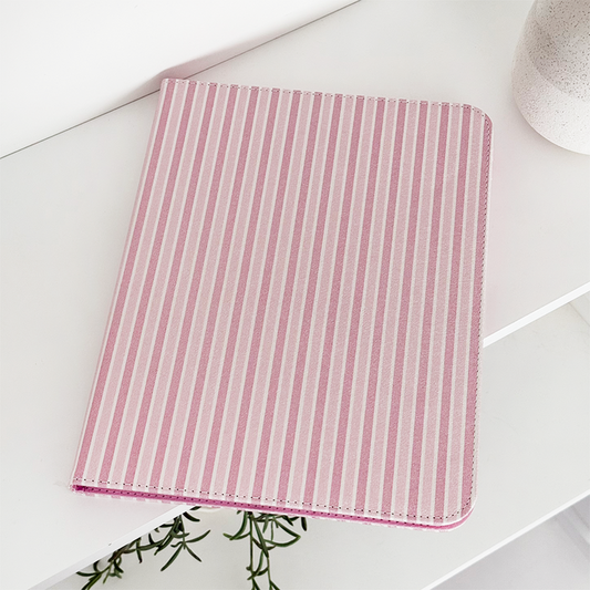 Pink and white striped Coconut Lane Powder Stripes iPad case, closed on a white shelf beside a small potted plant.