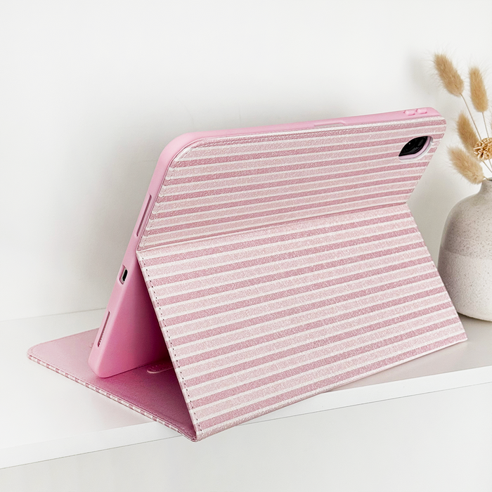 Pink vegan leather iPad case with white stripes, open beside dried flowers.