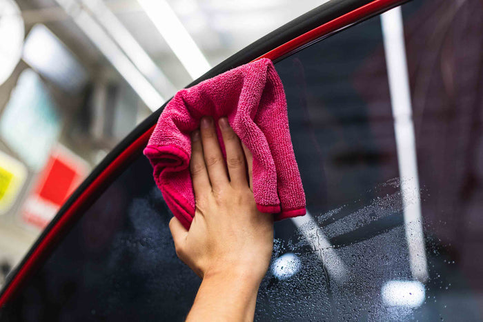 Person cleaning a car window with a pink FTW microfiber.