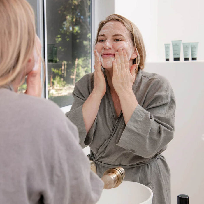 Woman applying cream to her face in front of a mirror.
