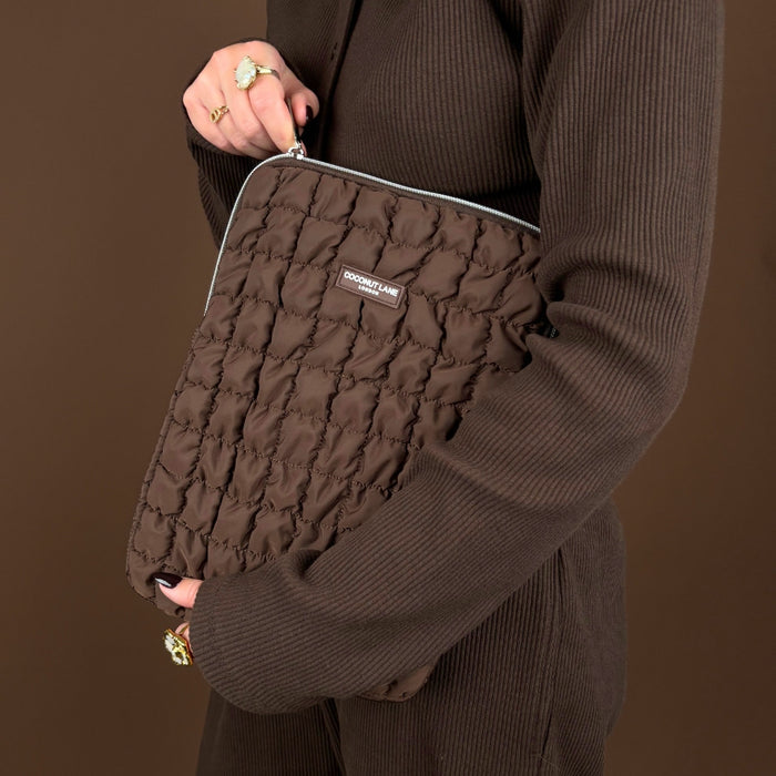 Person in a brown ribbed outfit holding a quilted chocolate-brown iPad sleeve with Coconut Lane branding, brown background.