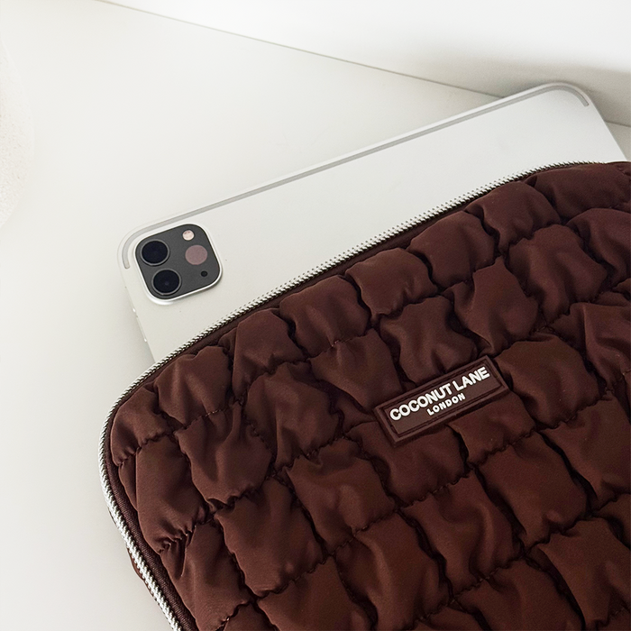 Tablet partially inside a brown quilted Coconut Lane iPad sleeve on a white surface.