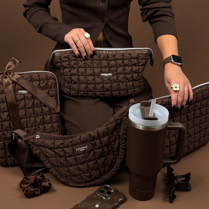 Woman in brown holds a quilted chocolate brown expandable makeup bag with matching accessories against a brown background.