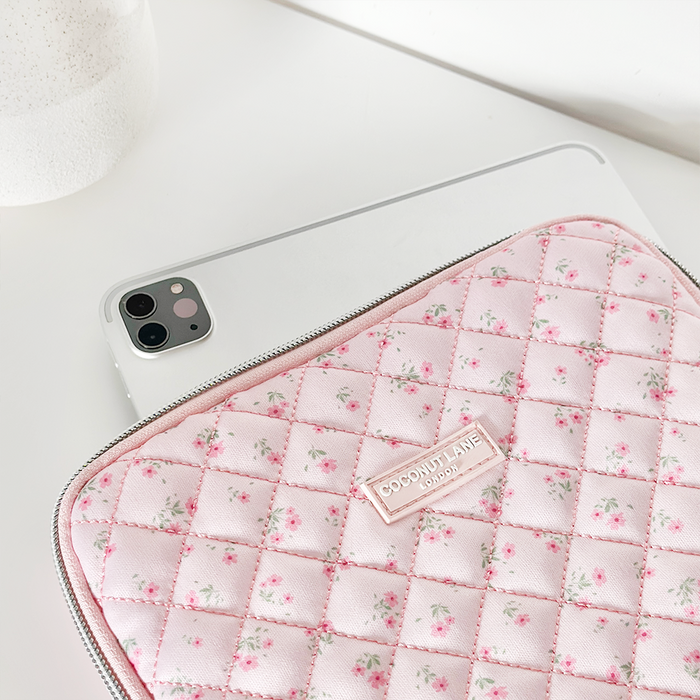 IPad partially slipped into a pink quilted floral Coconut Lane sleeve on a white surface.