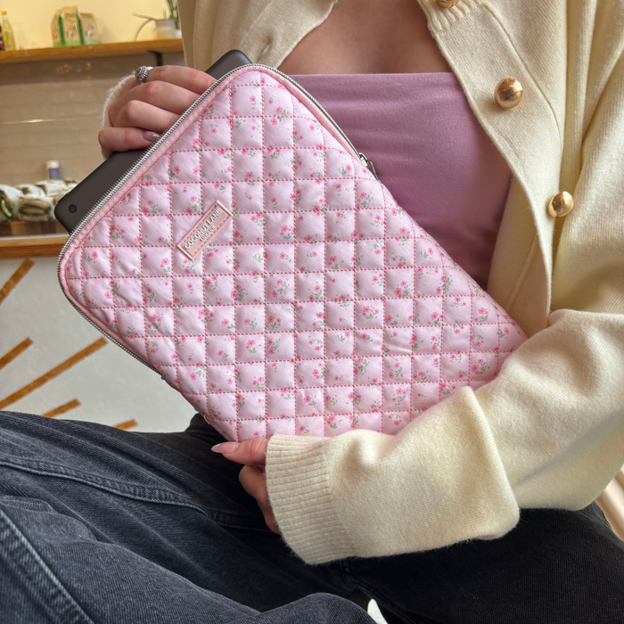 Person in a cream cardigan sits cross-legged holding a laptop and pink quilted floral Coconut Lane iPad sleeve.