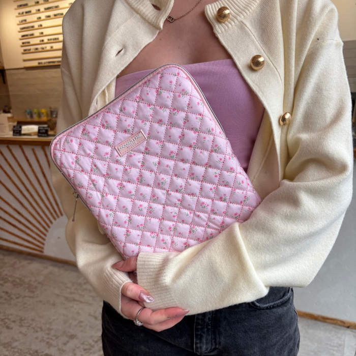 Woman in a cream cardigan holding a pink quilted iPad sleeve with ditsy floral pattern.