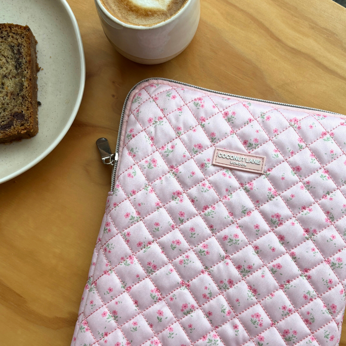 Pink quilted iPad sleeve with floral pattern on a table beside coffee and banana bread.