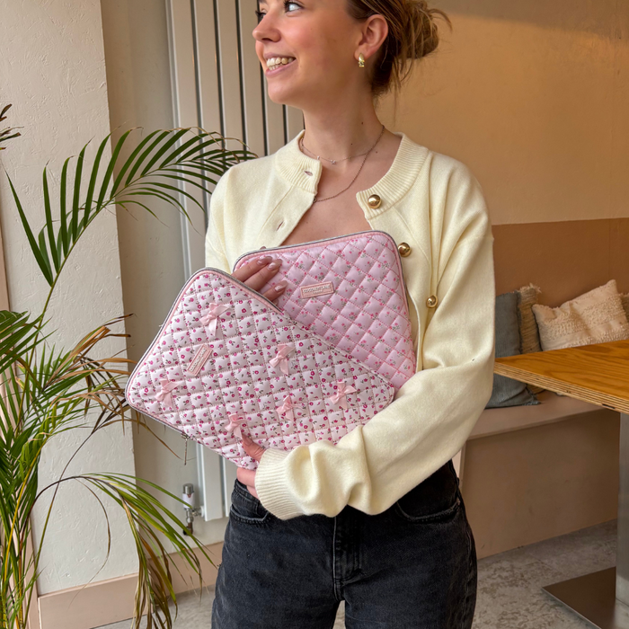 Woman in cream cardigan holds two quilted pink iPad sleeves with ditsy floral prints, standing indoors by a plant.