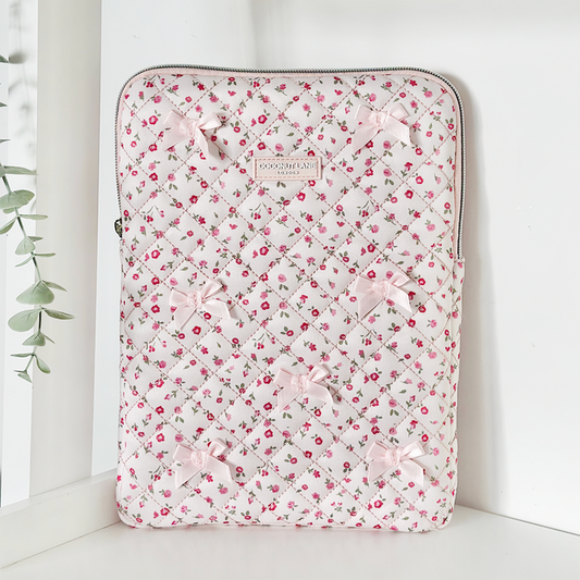 Quilted pink iPad sleeve with watercolour flower pattern and small bows, propped on a white shelf next to a plant.