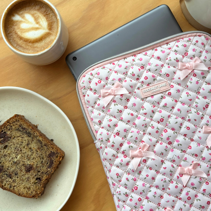 Latte, banana bread, and iPad in a pink quilted floral sleeve on a table.
