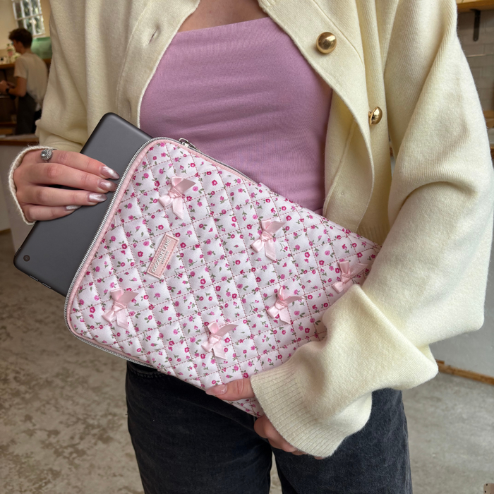 Person in a cream cardigan holds a tablet and a pink quilted iPad sleeve with watercolor flower pattern.