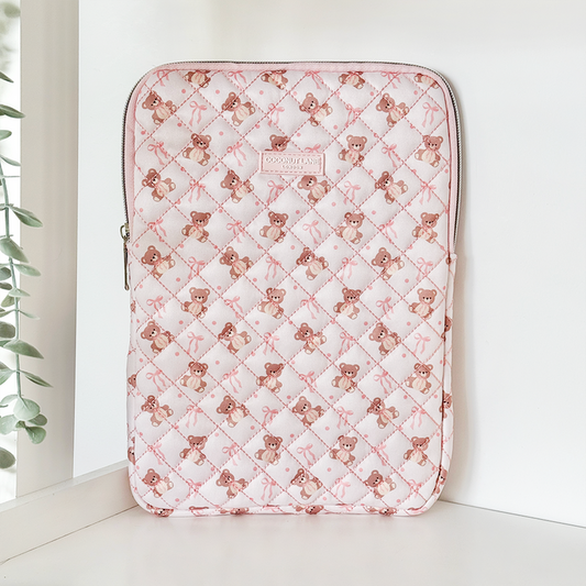 Pink quilted iPad sleeve with bow pattern, displayed upright on a white shelf.