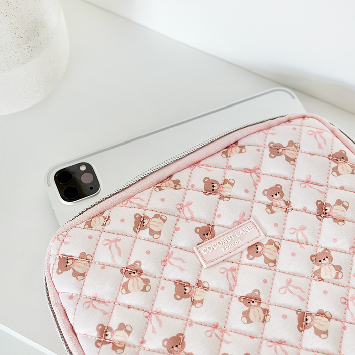 Silver iPhone next to a Coconut Lane brown quilted iPad sleeve with bow details on a white surface.