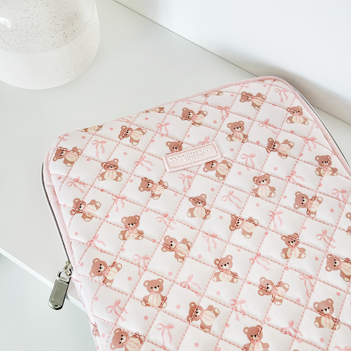 Pink quilted iPad sleeve with teddy and bow pattern next to a white vase.