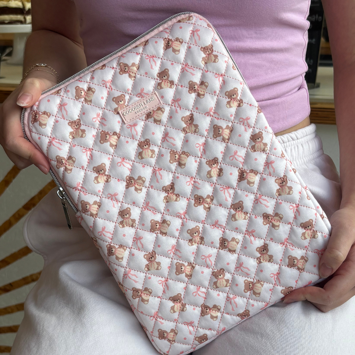 Person holding a quilted beige Thea Teddy iPad sleeve, dressed in a pink top and white pants.