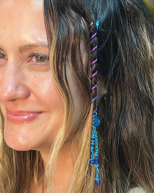 Close-up of a 4-inch rainbow Hair Twister spiral hair accessory with blue bead charm, worn in long wavy hair.