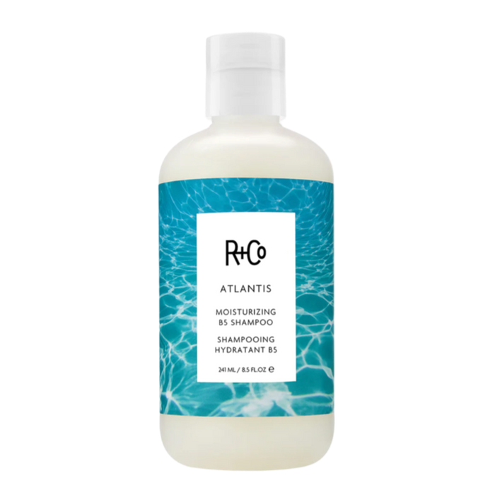 A bottle of R+Co ATLANTIS Moisturizing Shampoo with a white and blue label design.