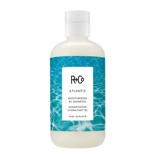 A bottle of R+Co ATLANTIS Moisturizing Shampoo with a white and blue label design.