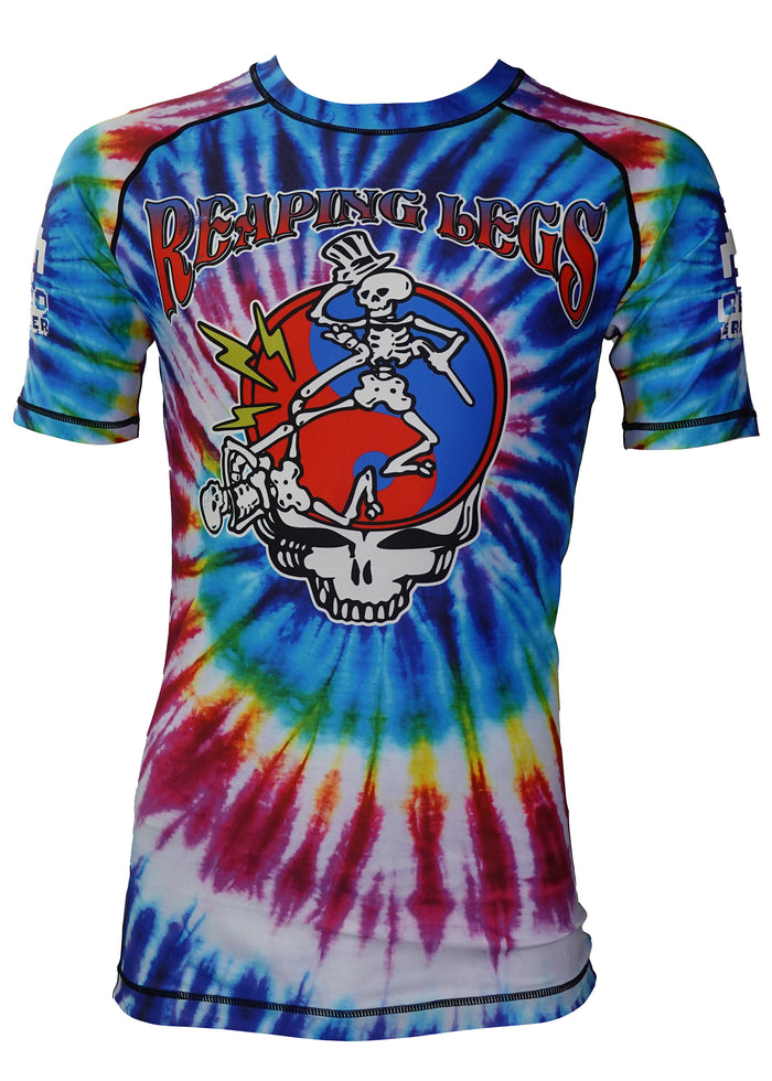 The Retro Grappler Reaping Leg Tye Dye Rash Guard features Reaping Legs text above skeletons grappling on a skull, set on a red/blue tie-dye background with colorful lightning in Grateful Dead-inspired style.