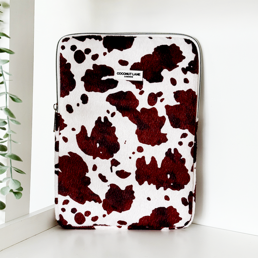 Brown and white cow print iPad sleeve with Rodeo Cowgirl design, standing upright next to a leafy green plant.
