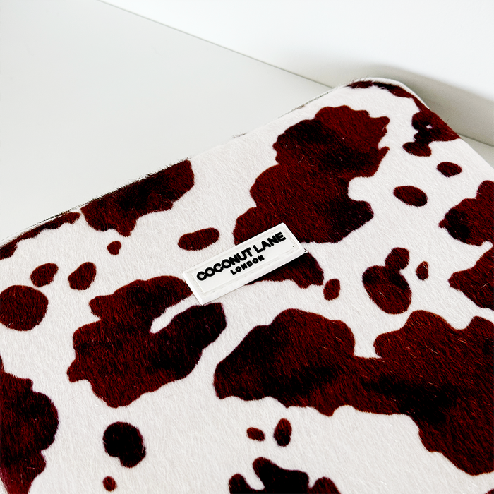 White iPad sleeve with dark brown cow print spots and front Coconut Lane branding.