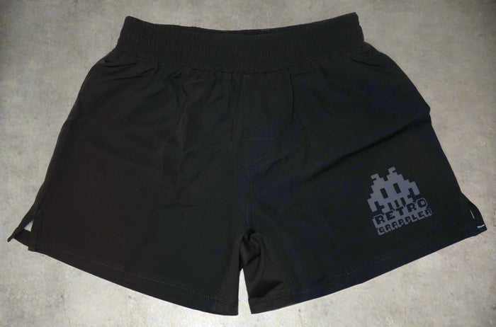 Simple Black Grappling Shorts by Retro Grappler, featuring an elastic waistband. A pixelated alien and the RETRO GRAPPLER text decorate the lower right leg. These lightweight BJJ shorts have no Velcro for ultimate training comfort.