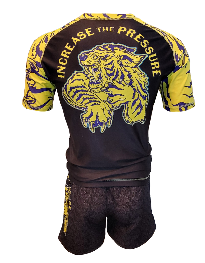 The Retro Grappler Tiger Pressure BJJ Rash Guard is a black and yellow athletic outfit with a roaring tiger graphic and INCREASE THE PRESSURE on the back. Matching shorts feature the same tiger design, ideal for grappling sessions.