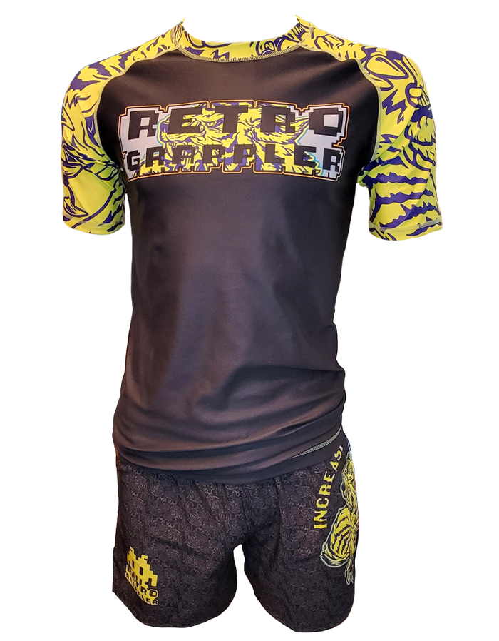 The Tiger Pressure Kit by Retro Grappler is a black and yellow short-sleeve BJJ rash guard and matching grappling shorts set, featuring bold graphic text and cartoon-style designs on the shoulders, sleeves, and leg.