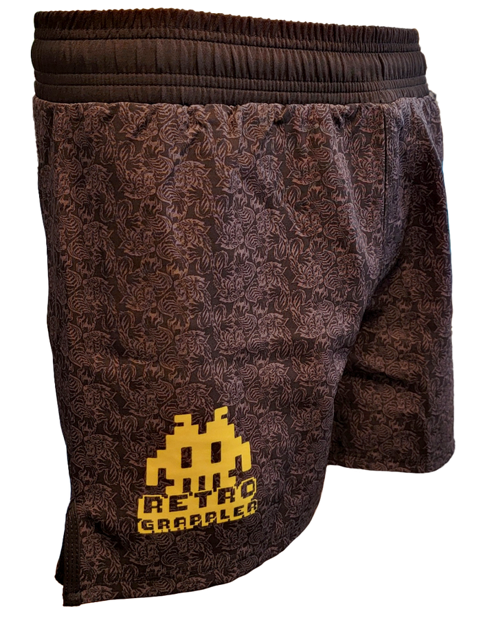 The Tiger Pressure Kit by Retro Grappler features brown grappling shorts with a subtle, intricate pattern and a yellow pixelated graphic plus Retro Grappler text on the lower left leg—ideal for pairing with your favorite BJJ rash guard.