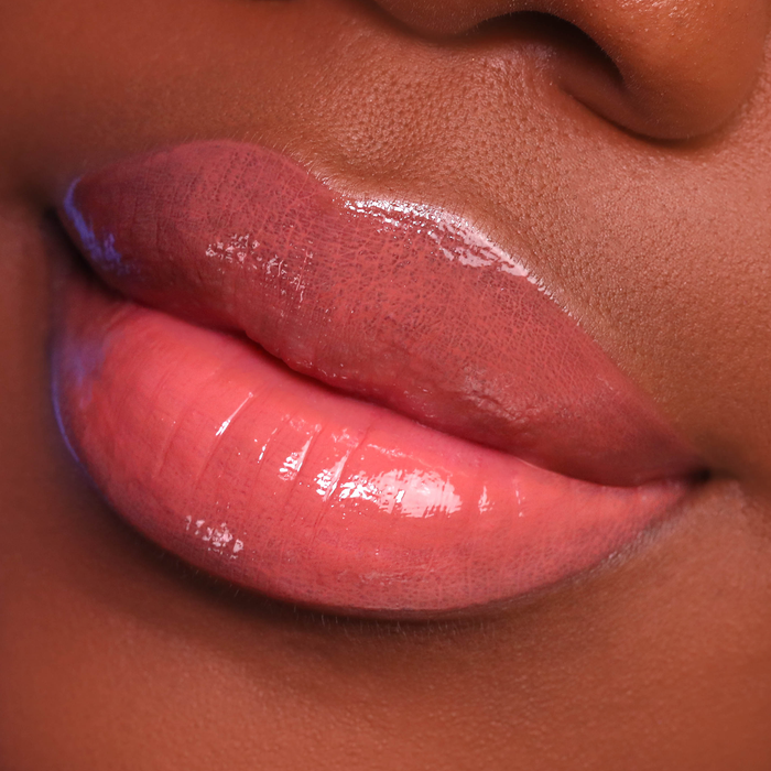 Vibes coral lip gloss on lips, deep skin tone close-up