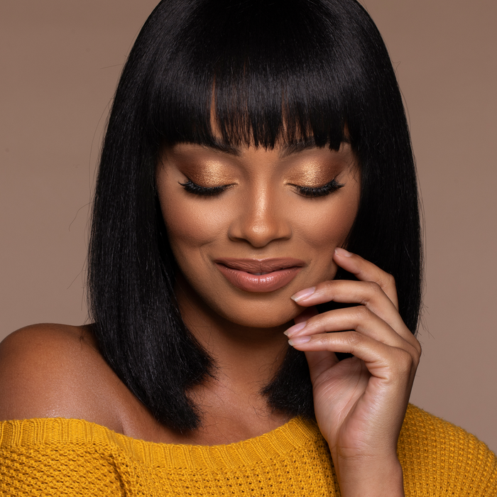 Model wearing Vibes lip gloss in a mustard off-shoulder top, smiling with eyes closed