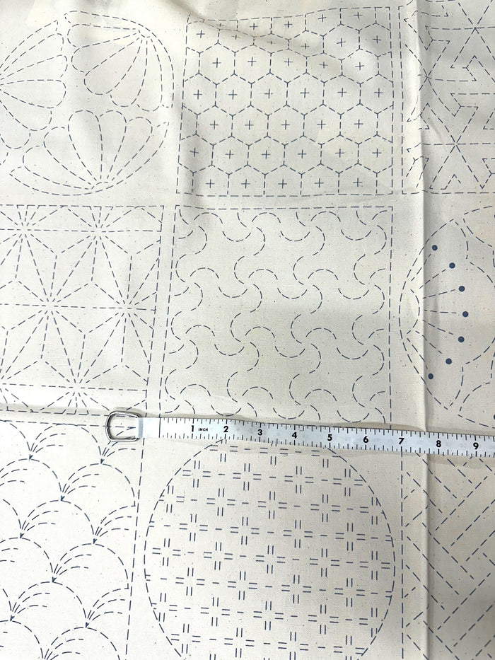 cream colored fabric with sashiko design squares printed on it with a measuring tape on top