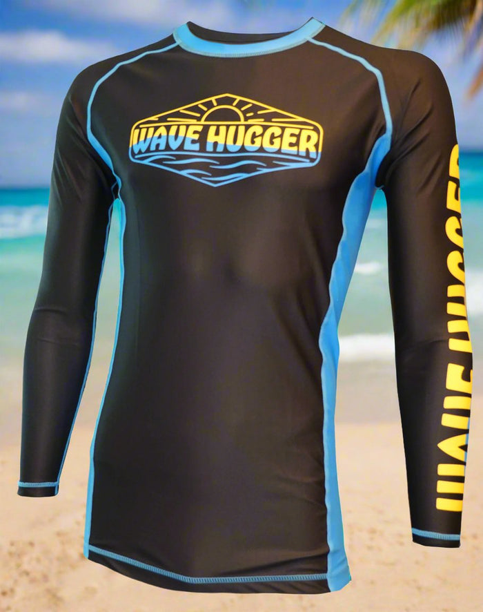The Wave Hugger Blue Panel Rash Guard is a black and blue long-sleeve Lycra top with WAVE HUGGER in yellow on the chest and sleeve, showcased against a scenic beach with sand, ocean, and palm trees.