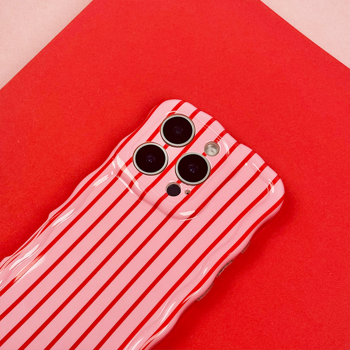 Pink phone in a Coconut Lane wavy case with red and white cherry stripe pattern, set on a red and pale pink background.